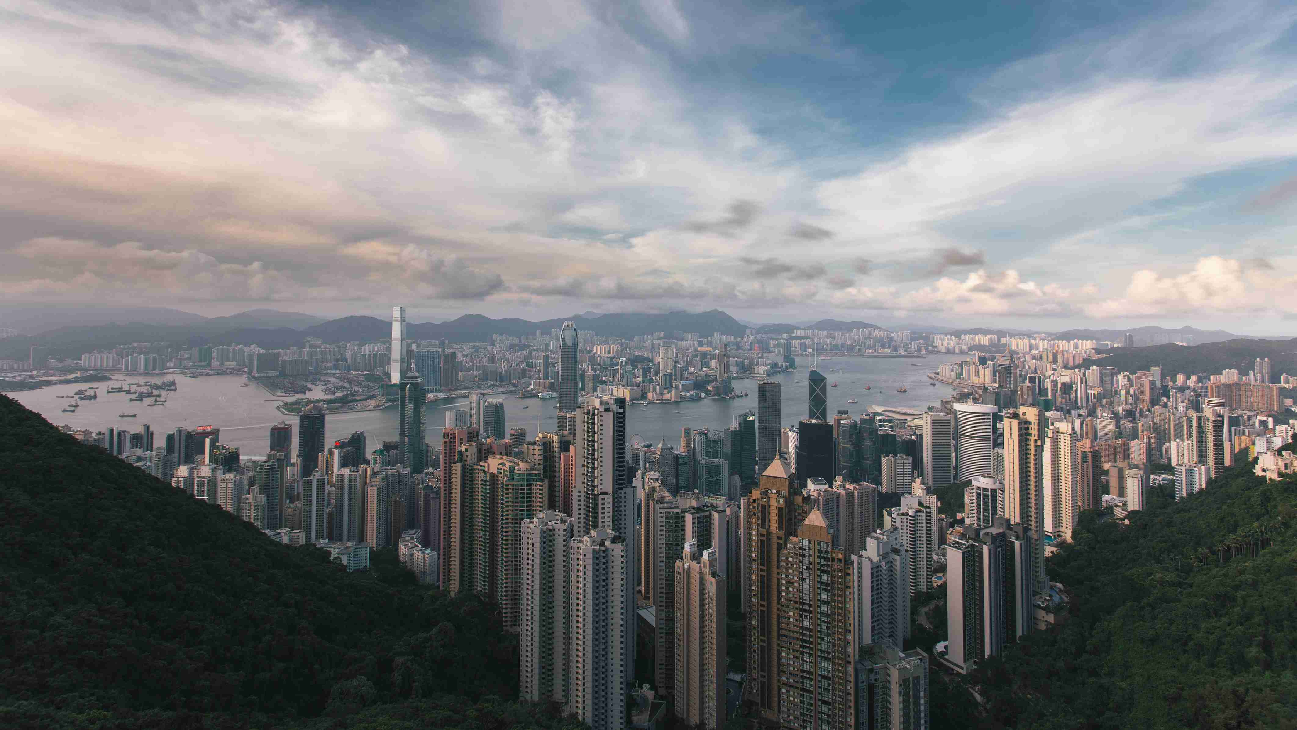 Aerial view of dense city skyline with skyscrapers, harbor, and surrounding mountains
