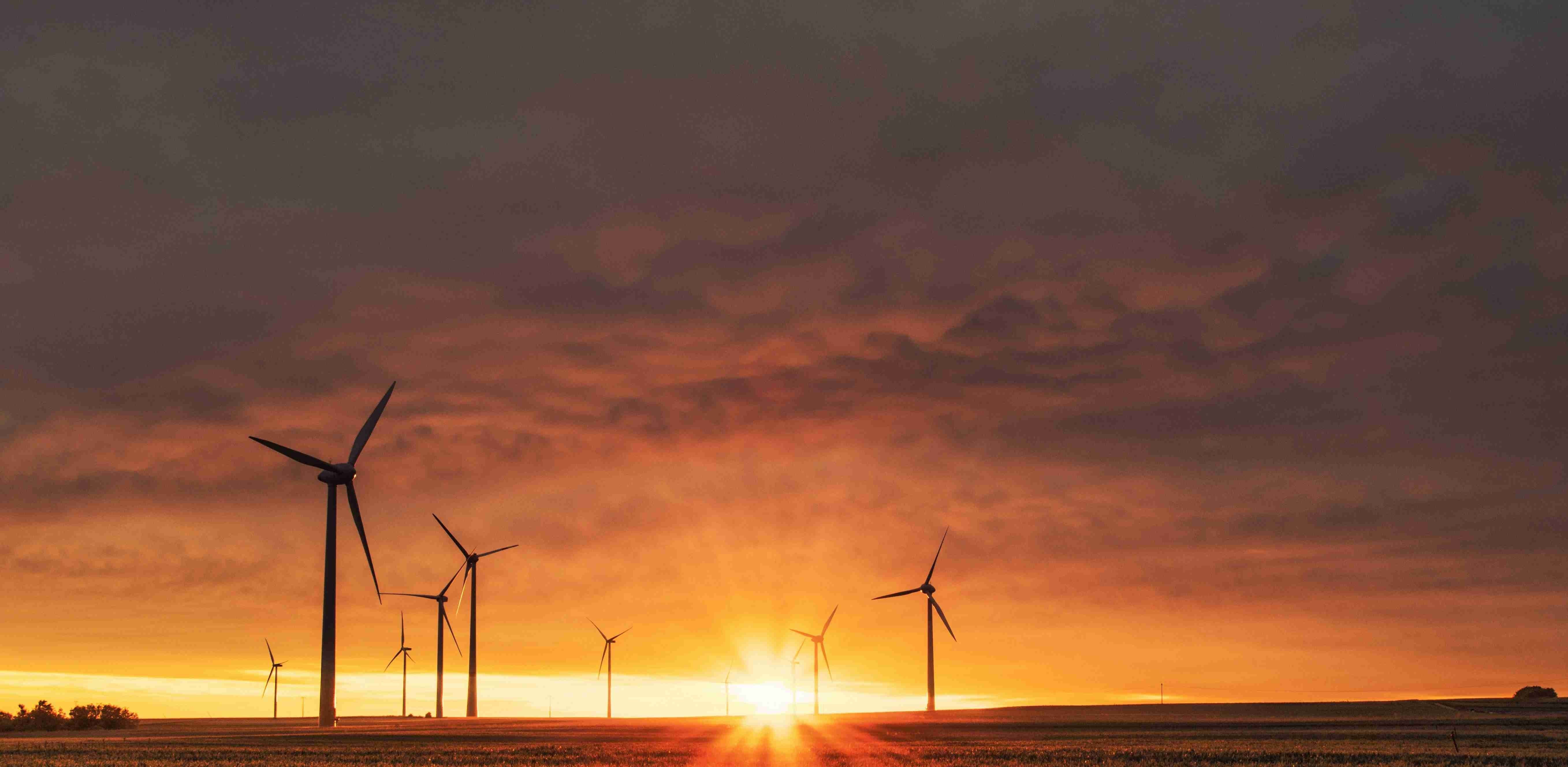 Wind turbines on farmland at sunset with orange and purple clouds