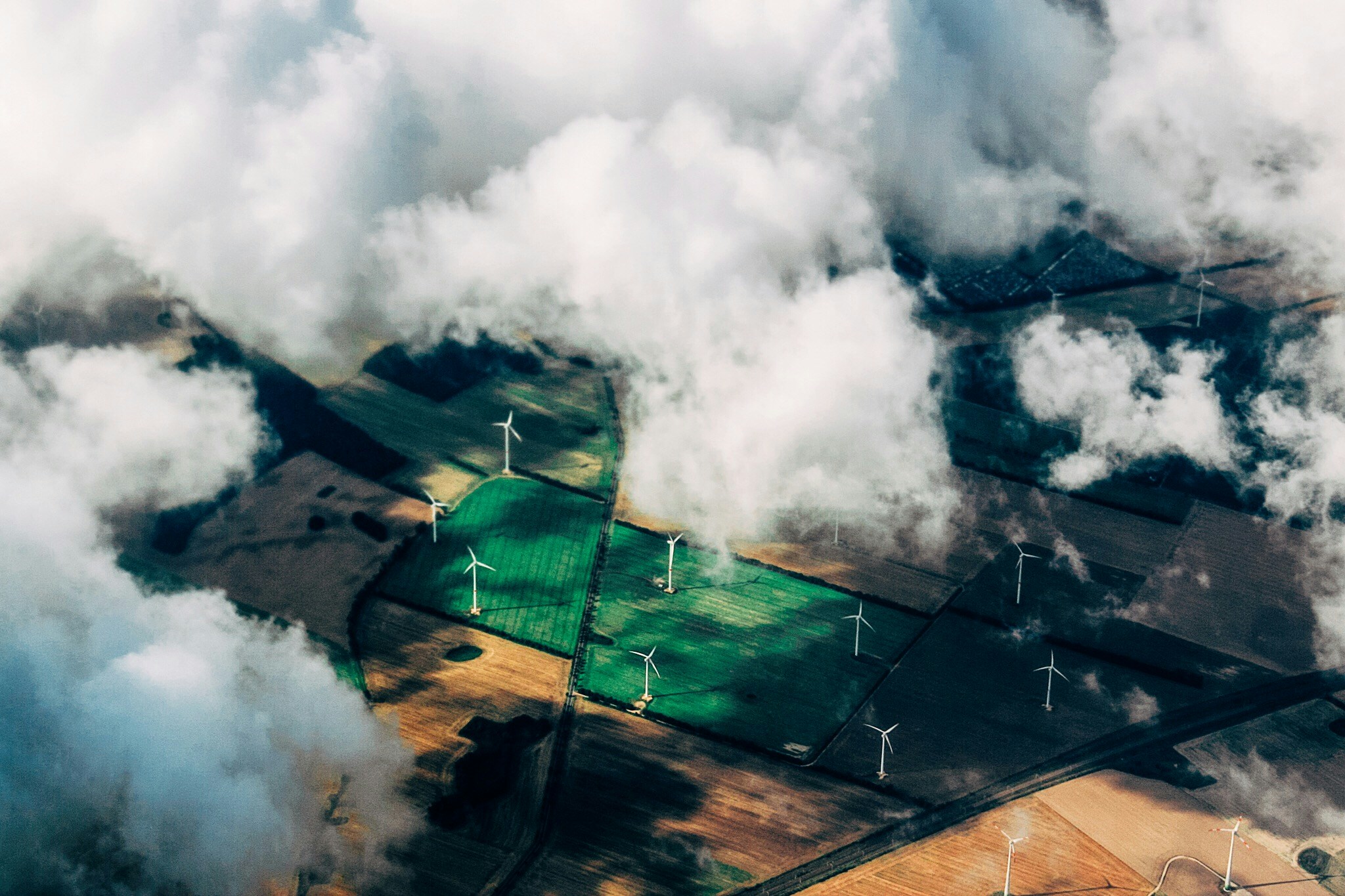 Aerial view of farmland with wind turbines partly covered by clouds.