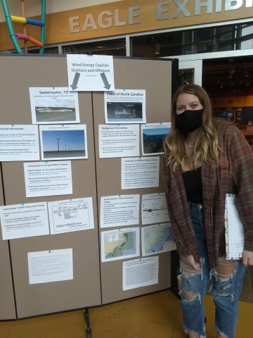 A masked student poses in front of a research poster presentation