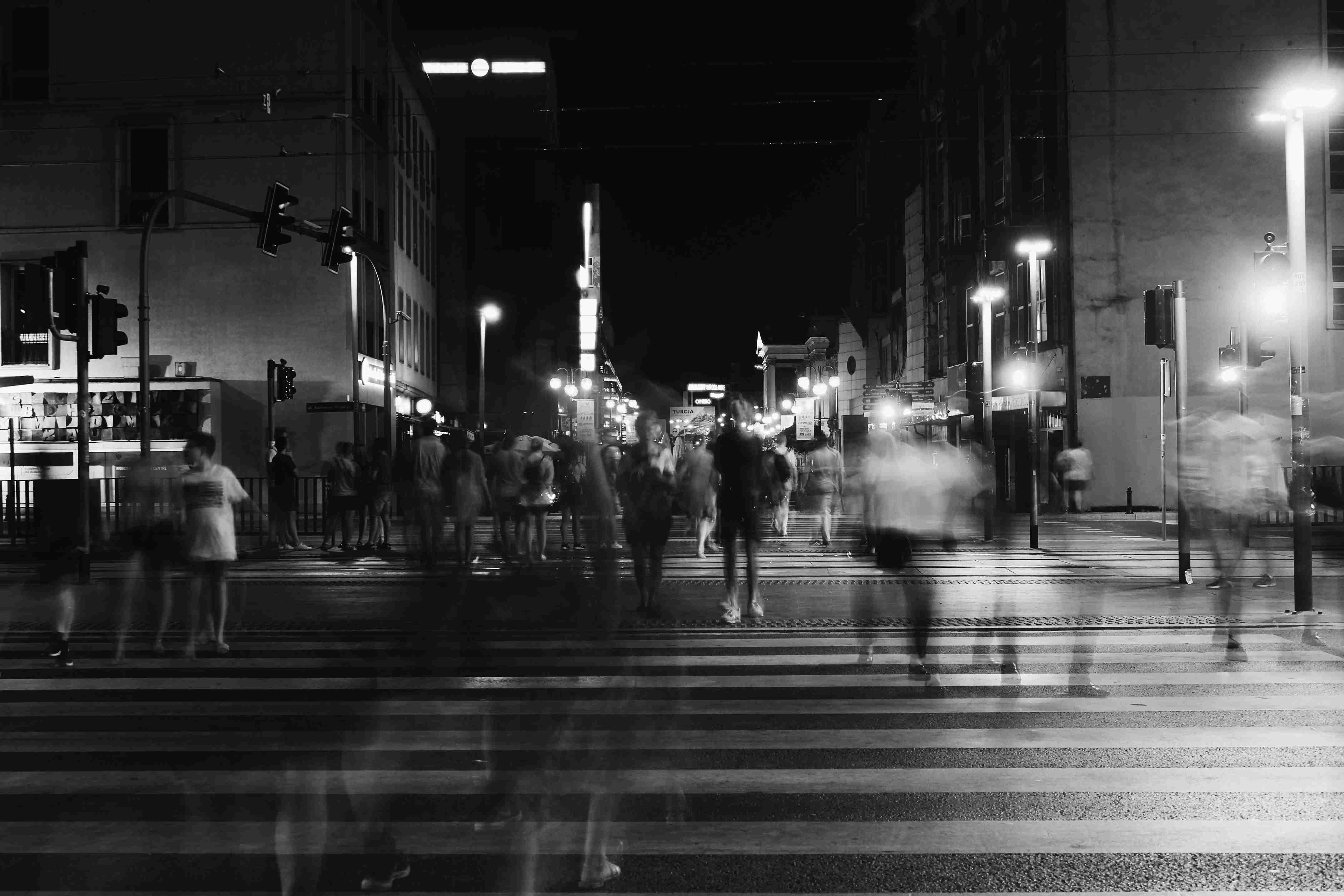 Black-and-white photo of people crossing a city street at night with blurred motion